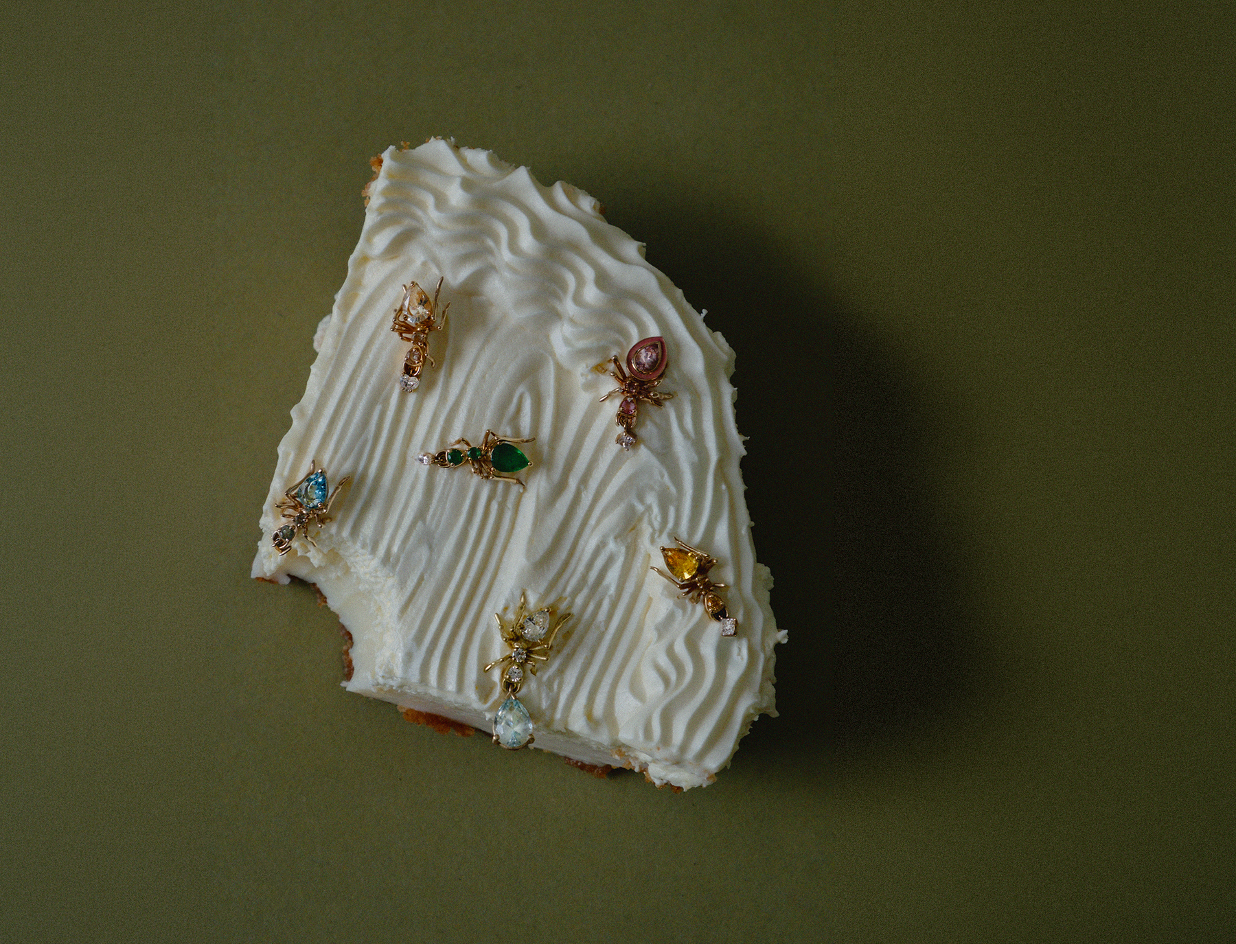 A small irregular white cake slice topped with piped cream and kokoro stud earrings in 14k yellow gold
