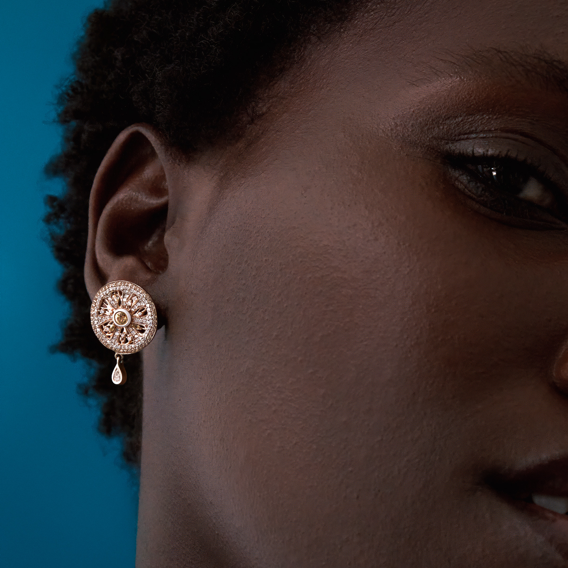 Close-up of a woman wearing a decorative earring against a blue background