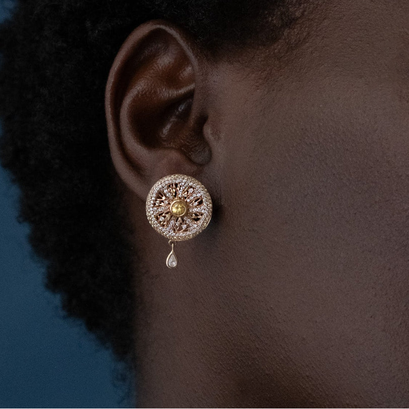 Close-up of an ear wearing a decorative earring with a blue background