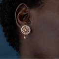 Close-up of an ear wearing a decorative earring with a blue background