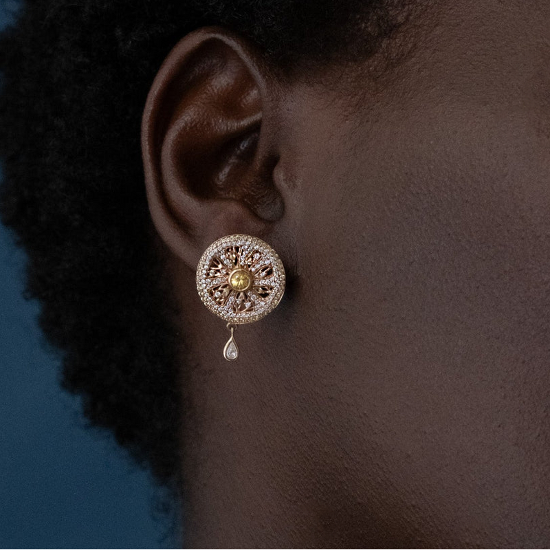 Close-up of an ear wearing a decorative earring with a blue background